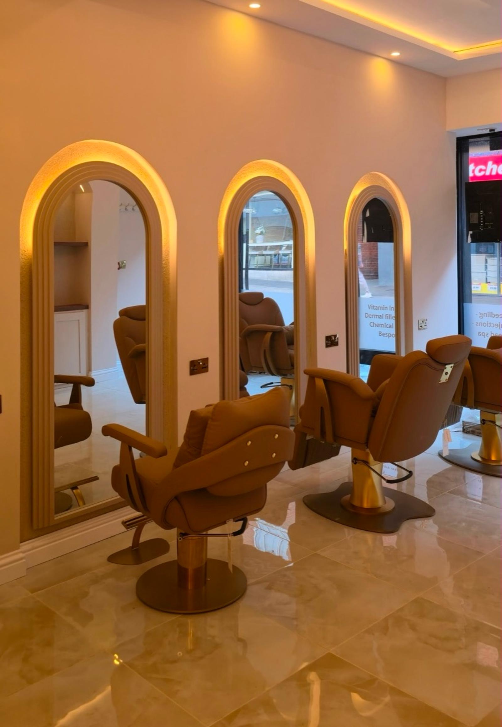 Three gold-lit arched mirrors with camel salon chairs on a polished marble floor